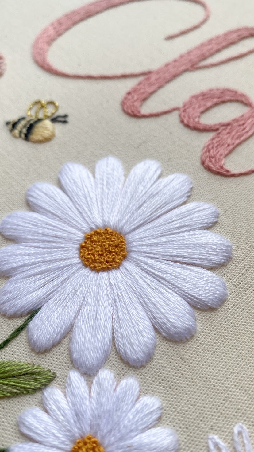 Detalhe de margaridas bordadas com abelha e letra em rosa